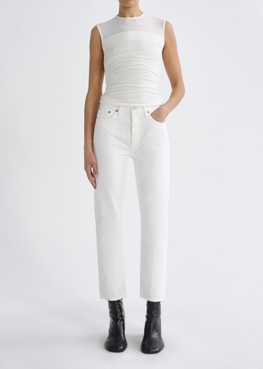 Person wearing a white sleeveless ruched top with white straight leg jeans and black ankle boots on a grey background