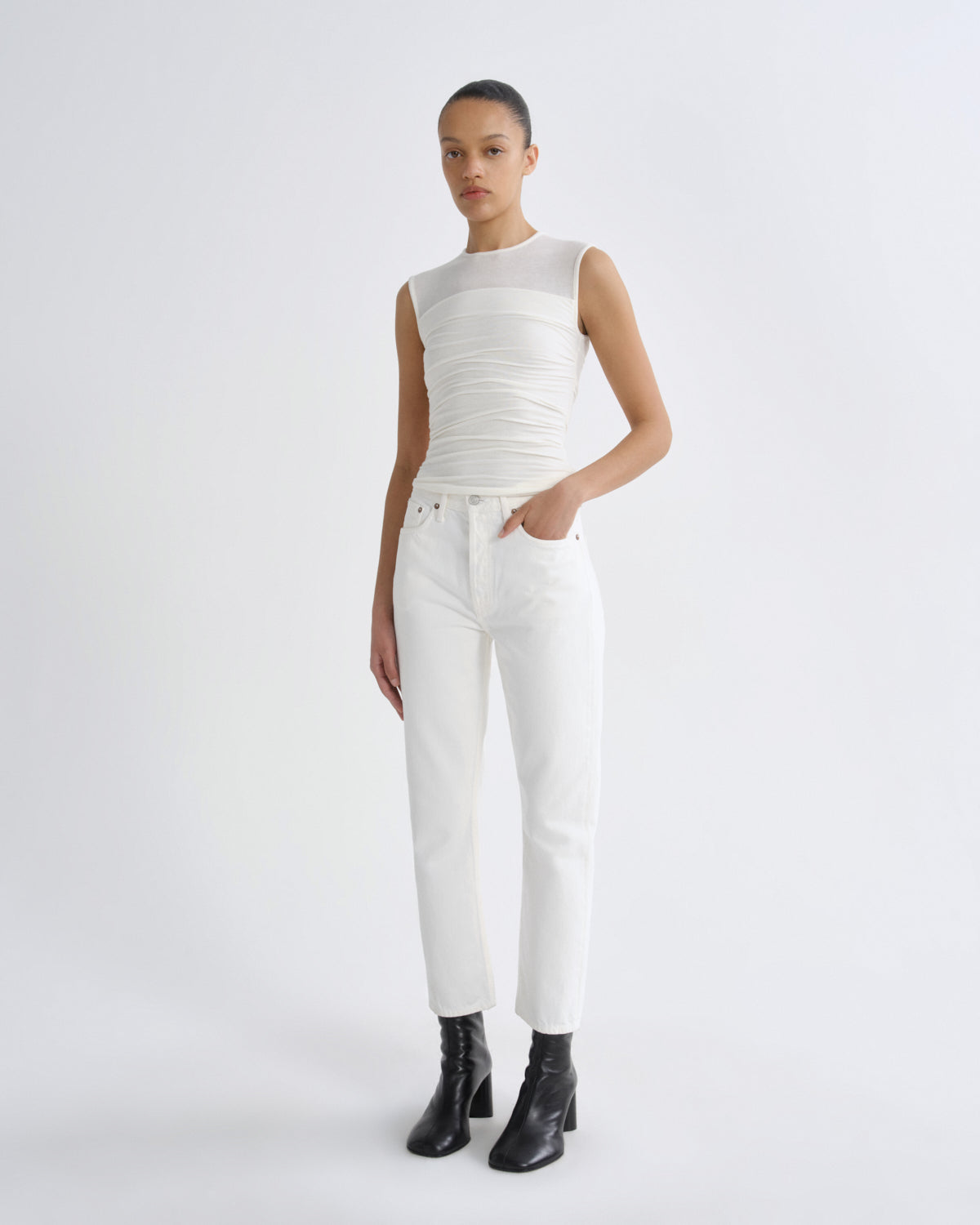 Person wearing a white sleeveless top and pants with black boots on a white background