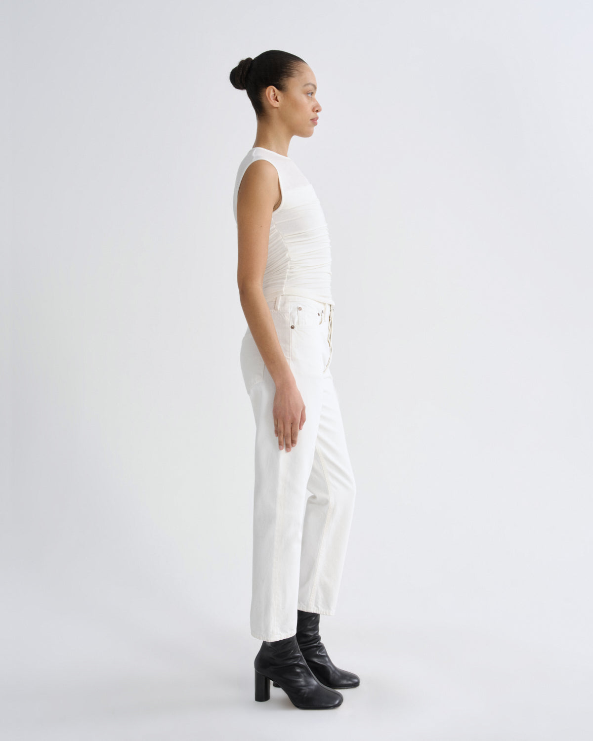 Woman wearing a white sleeveless top and pants with black shoes on a light gray background