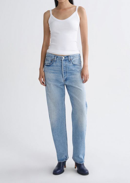 Person wearing a white tank top and light blue jeans on a grey background.