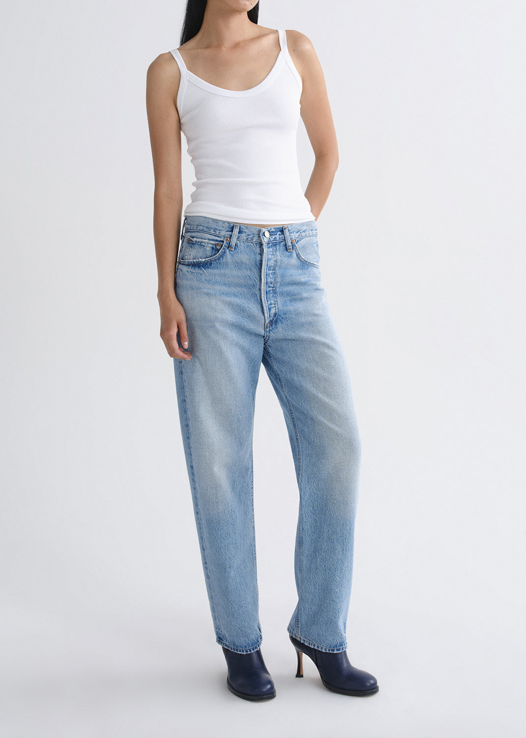 Person wearing a white tank top and light blue jeans on a grey background.