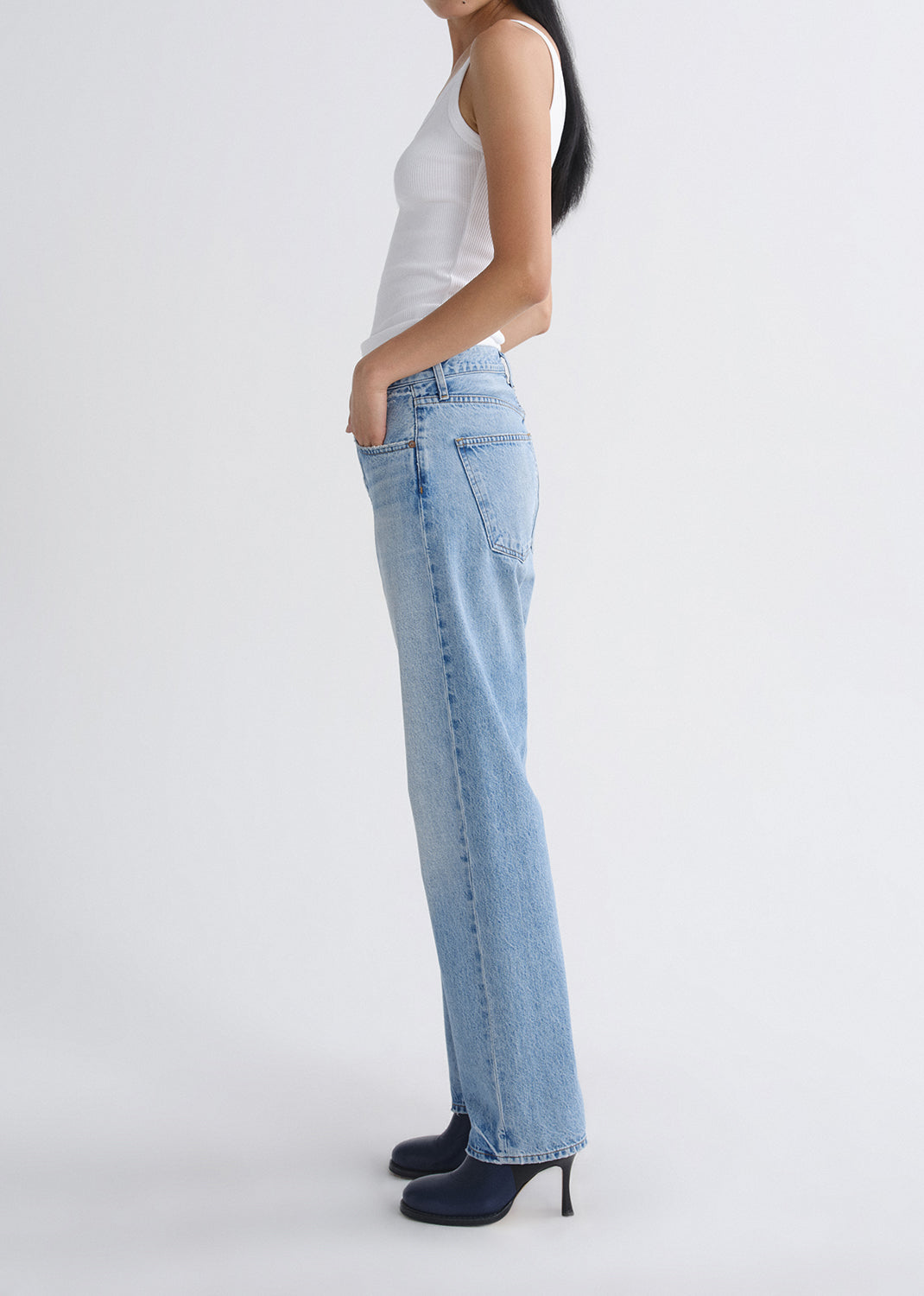Person wearing light blue jeans and a white top on a grey background.