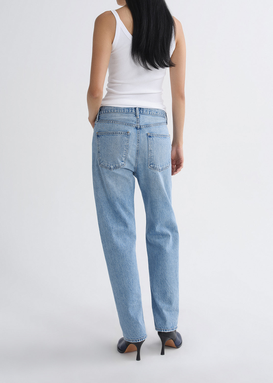 Person wearing light blue jeans and a white top on a grey background.