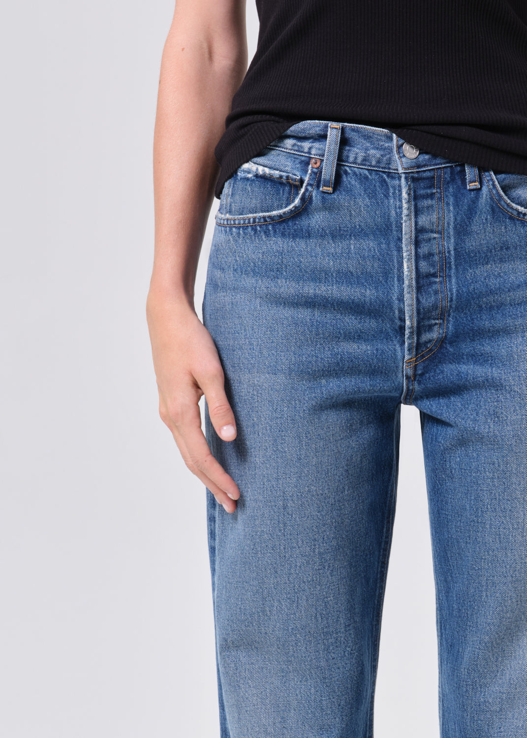 Person wearing blue jeans and a black top on a light gray background