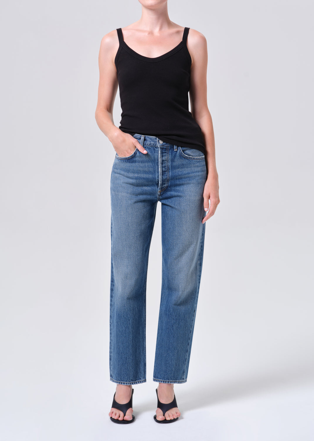 Person wearing a black tank top and blue jeans on a white background