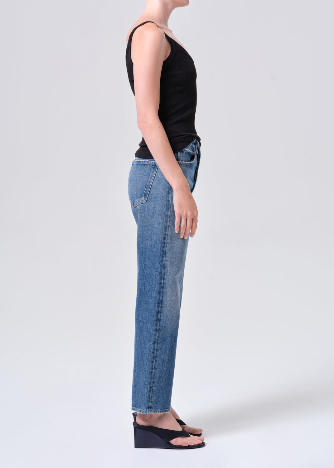 Person wearing blue jeans and a black top on a white background