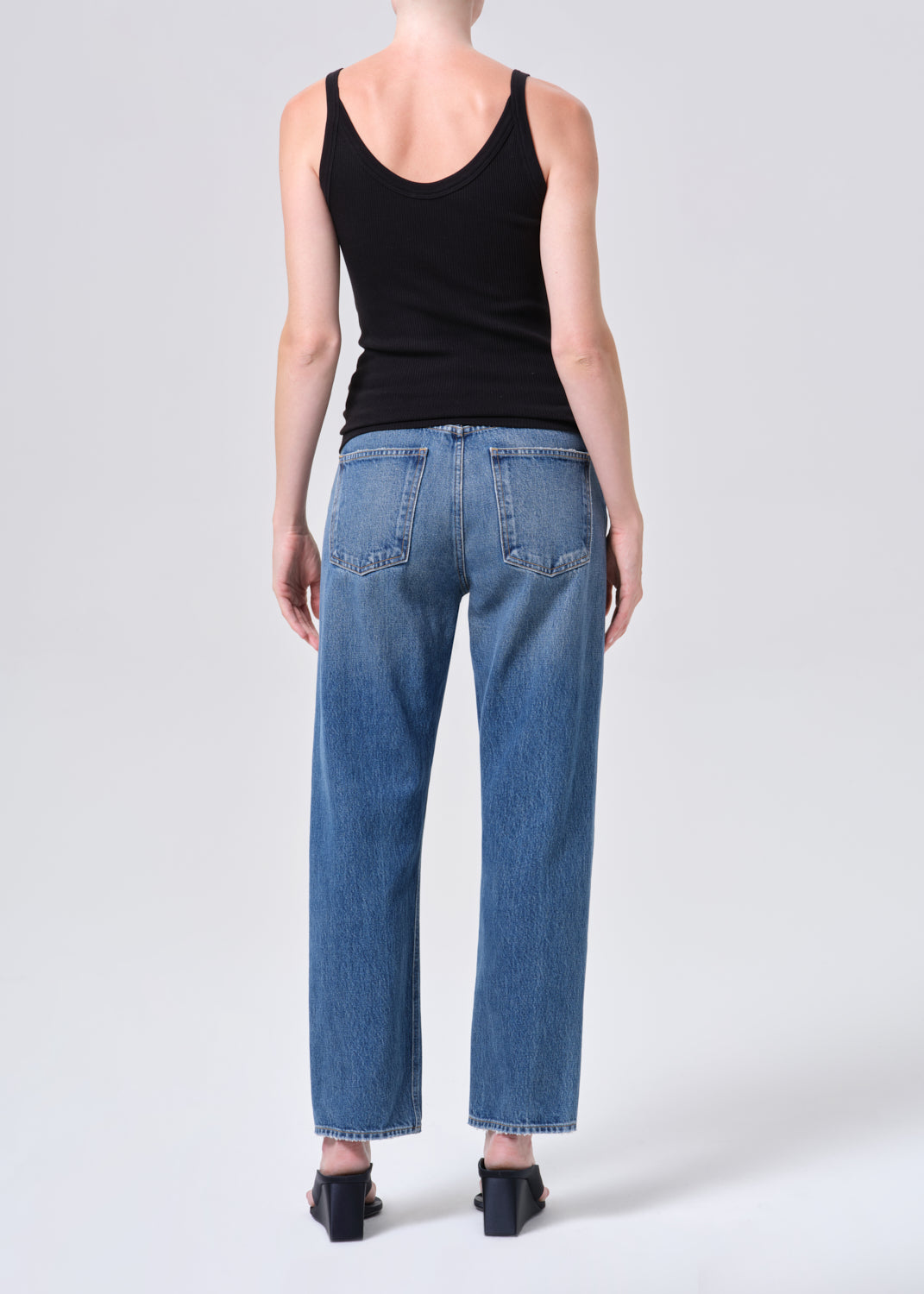 Person wearing a black tank top and blue jeans on a white background