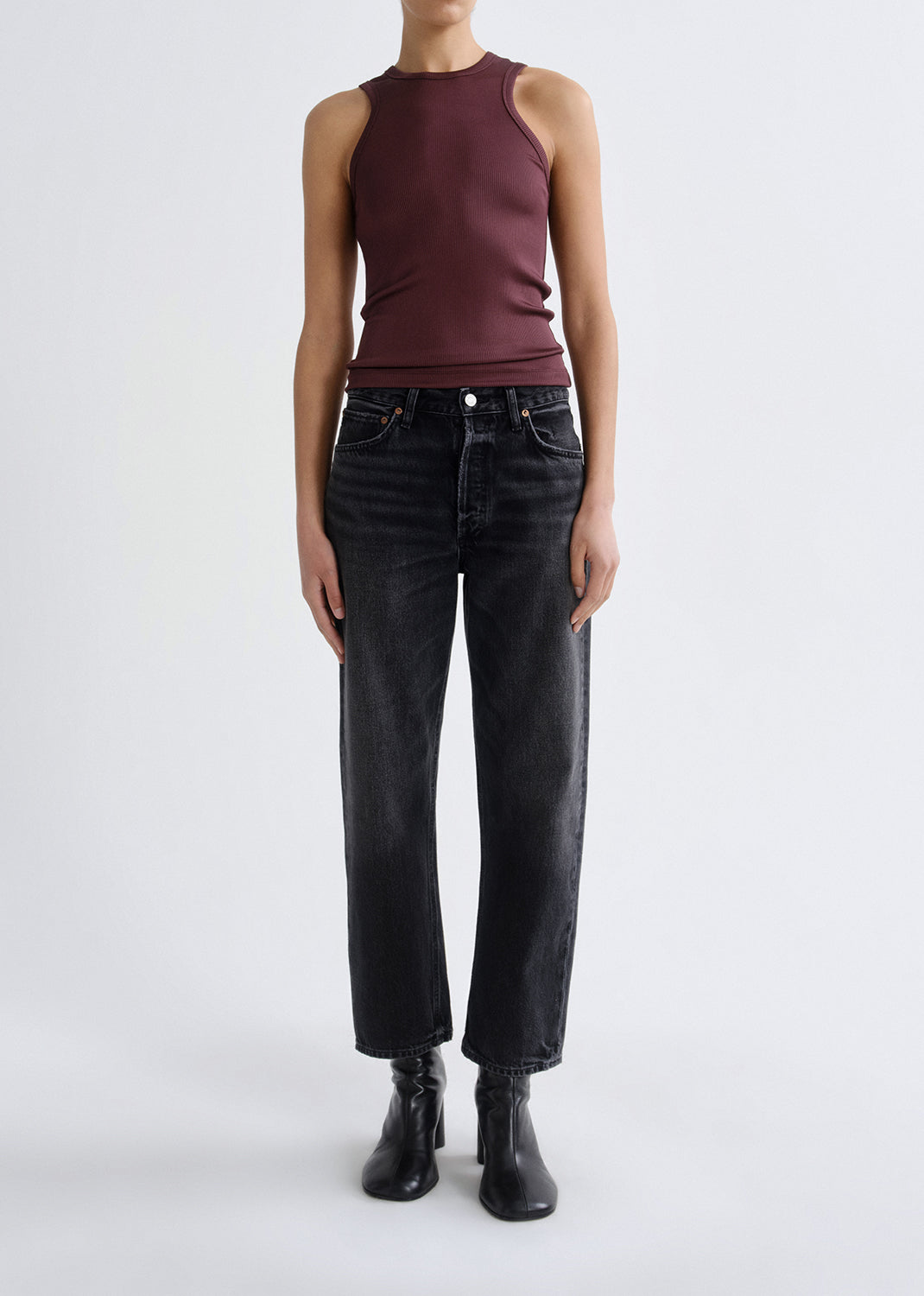A model wearing a sleeveless burgundy ribbed tank top, black wide-leg cropped jeans, and black ankle boots, standing against a grey background.