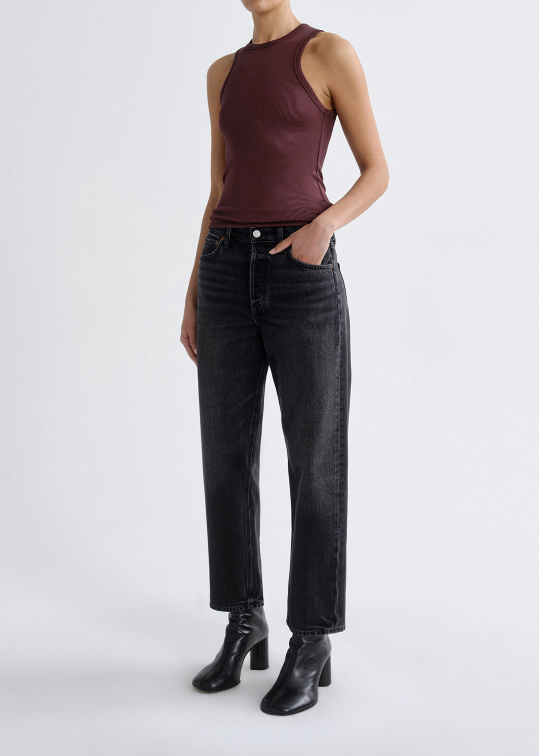 A model wearing a sleeveless dark burgundy top, black wide-leg jeans, and black leather ankle boots, standing against a grey background.