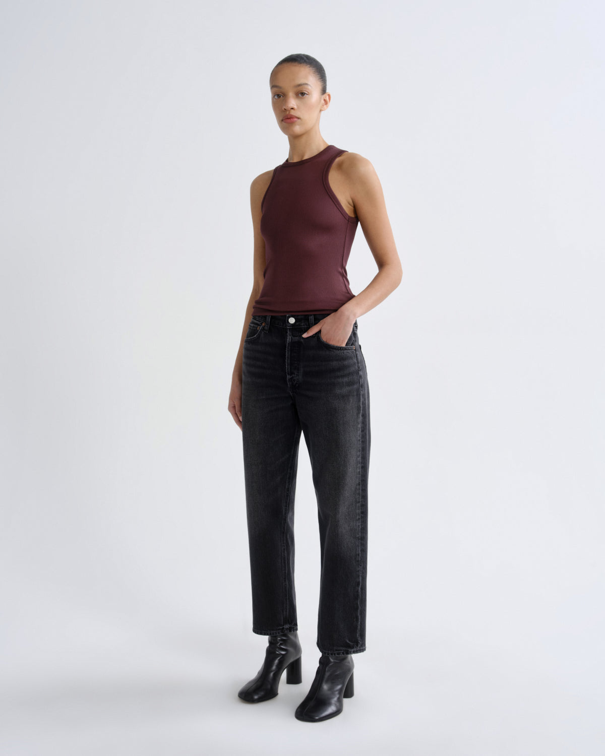 Woman wearing a burgundy halter top and black jeans on a white background