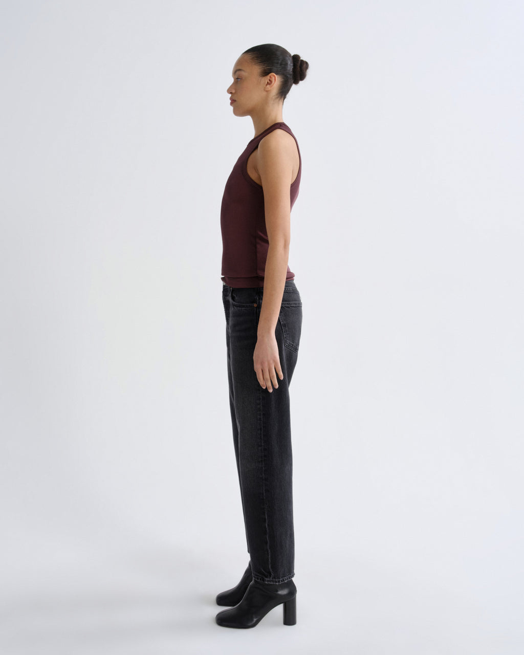 Woman wearing a burgundy top and black pants standing against a white background