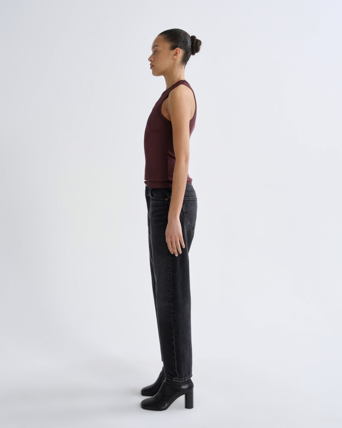 Woman wearing a burgundy top and black pants standing against a white background
