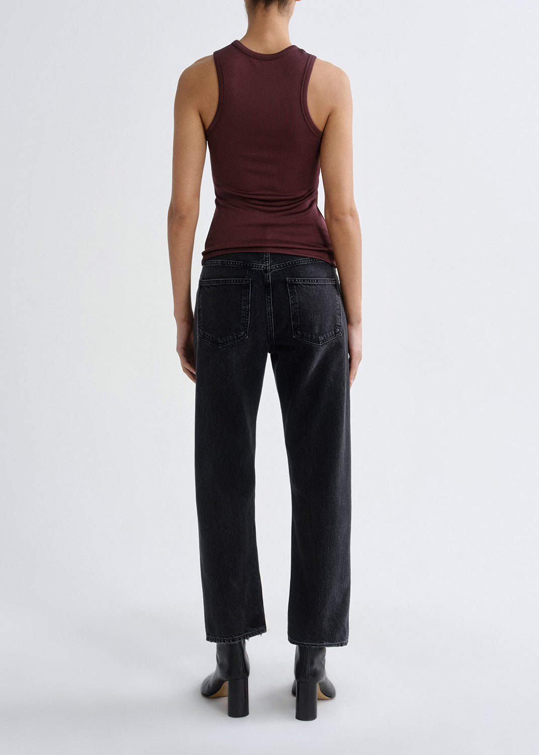 A model shown from the back wearing a sleeveless dark burgundy top and black wide-leg jeans with black ankle boots, set against a grey background.