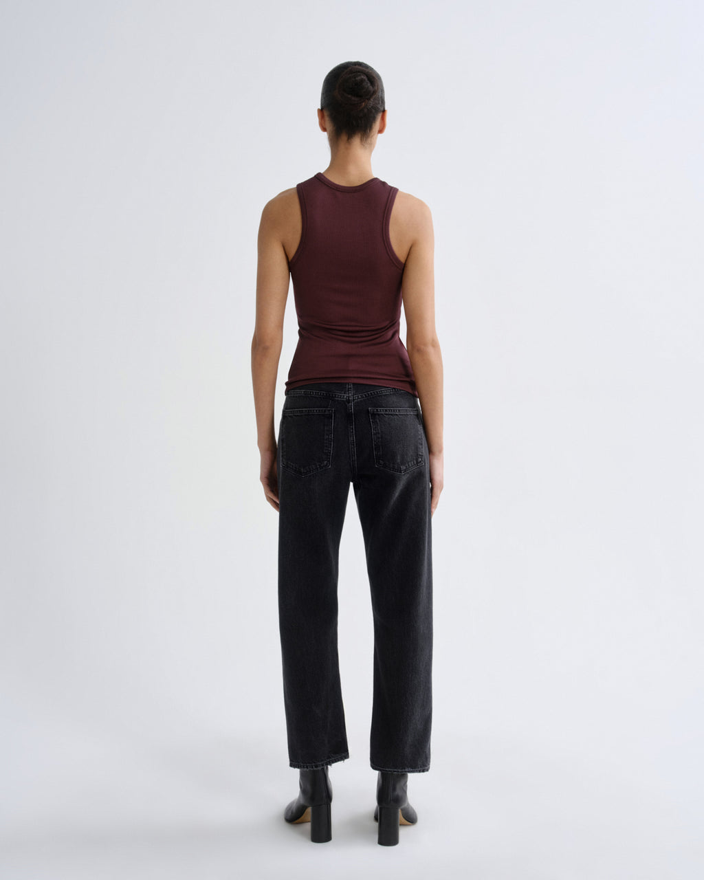 Person wearing a brown tank top and black pants on a white background