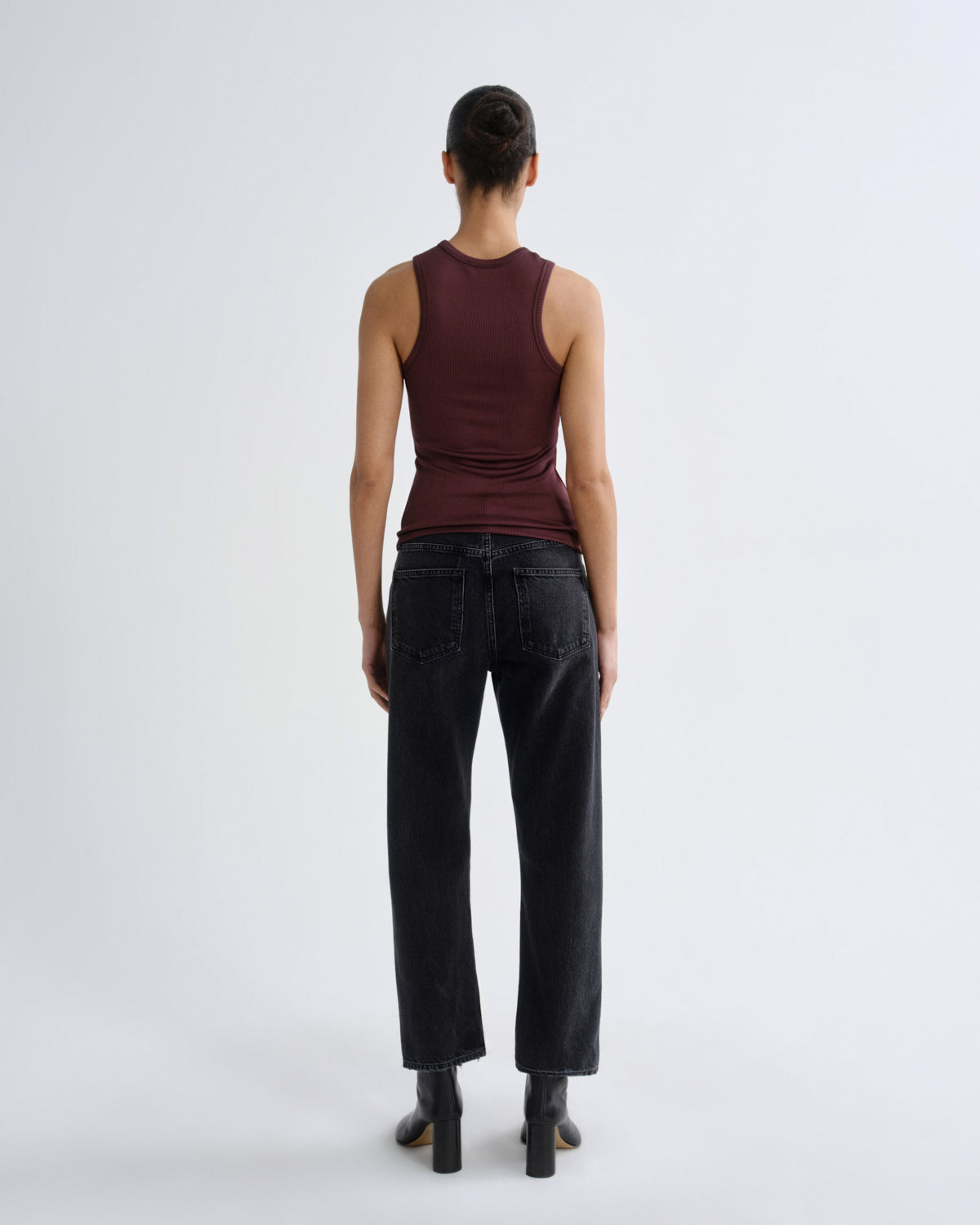 Person wearing a brown tank top and black pants on a white background