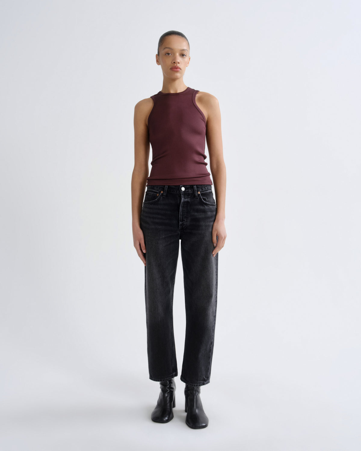 Person wearing a burgundy sleeveless top and black jeans on a white background
