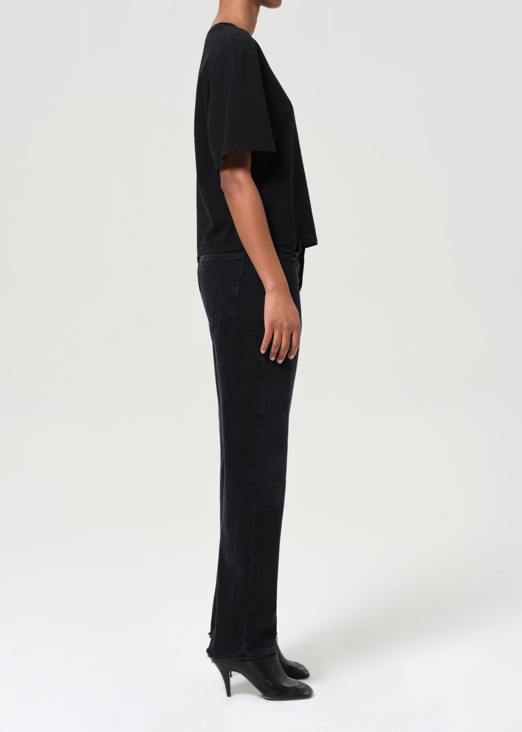 Person wearing a black outfit with high-waisted pants and black shoes on a white background