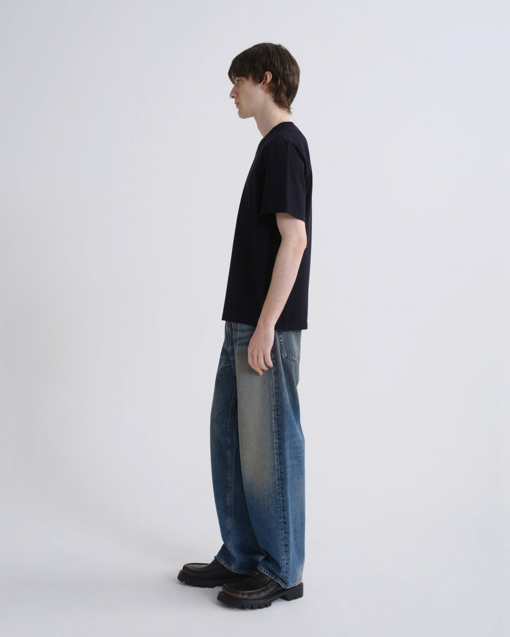 Person wearing a black t-shirt and blue jeans standing against a white background
