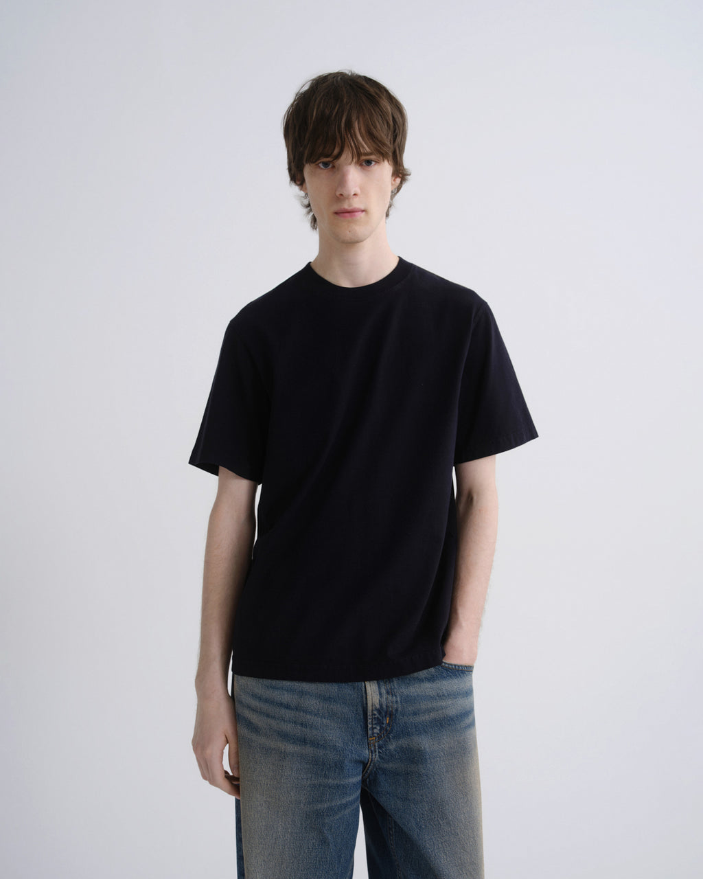 Person wearing a black t-shirt and blue jeans against a plain background