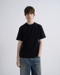 Person wearing a black t-shirt and blue jeans against a plain background
