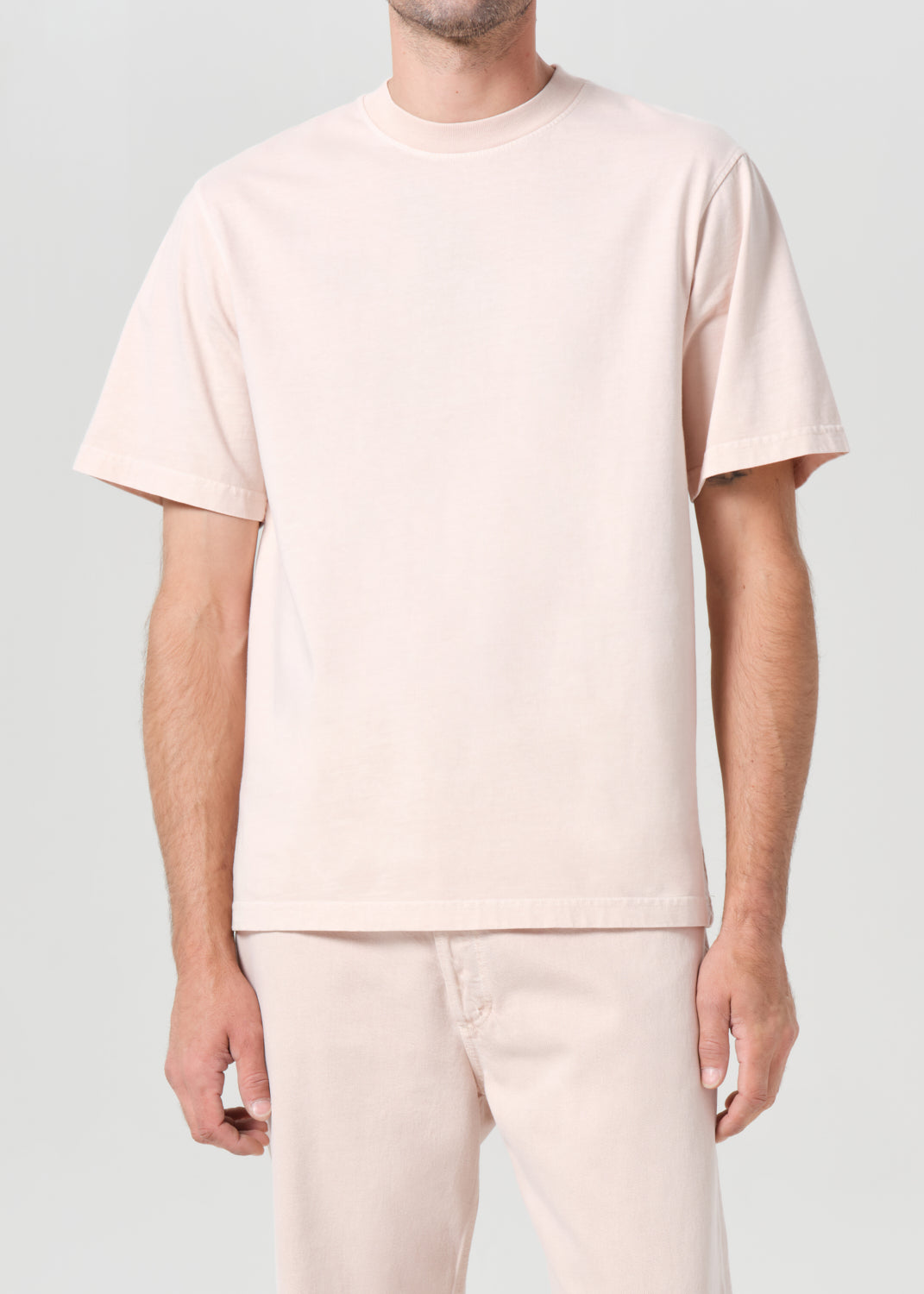 Person wearing a light pink t-shirt and pants on a plain background