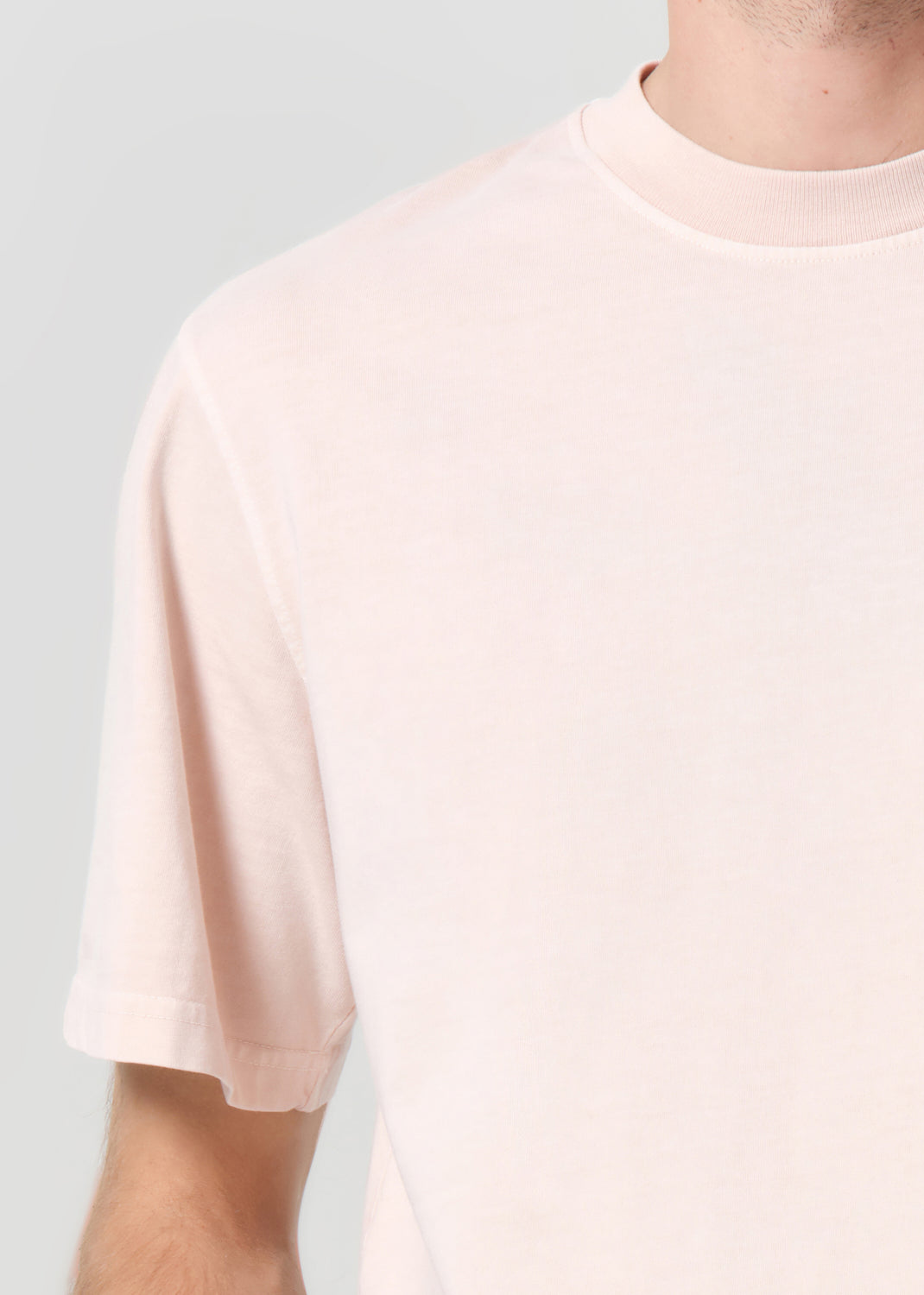 Person wearing a light pink t-shirt against a plain background