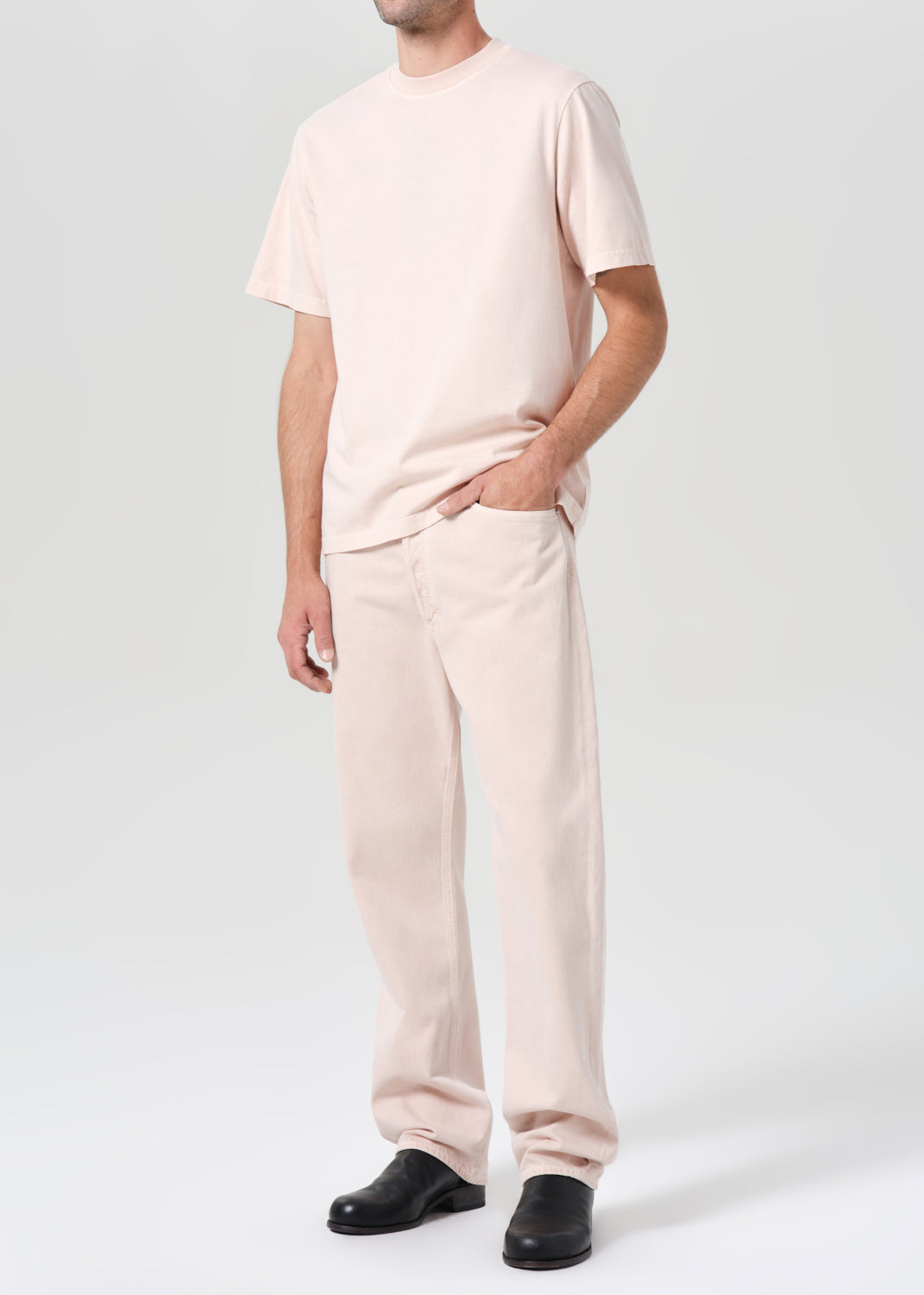 Person wearing a light pink outfit with black shoes on a white background