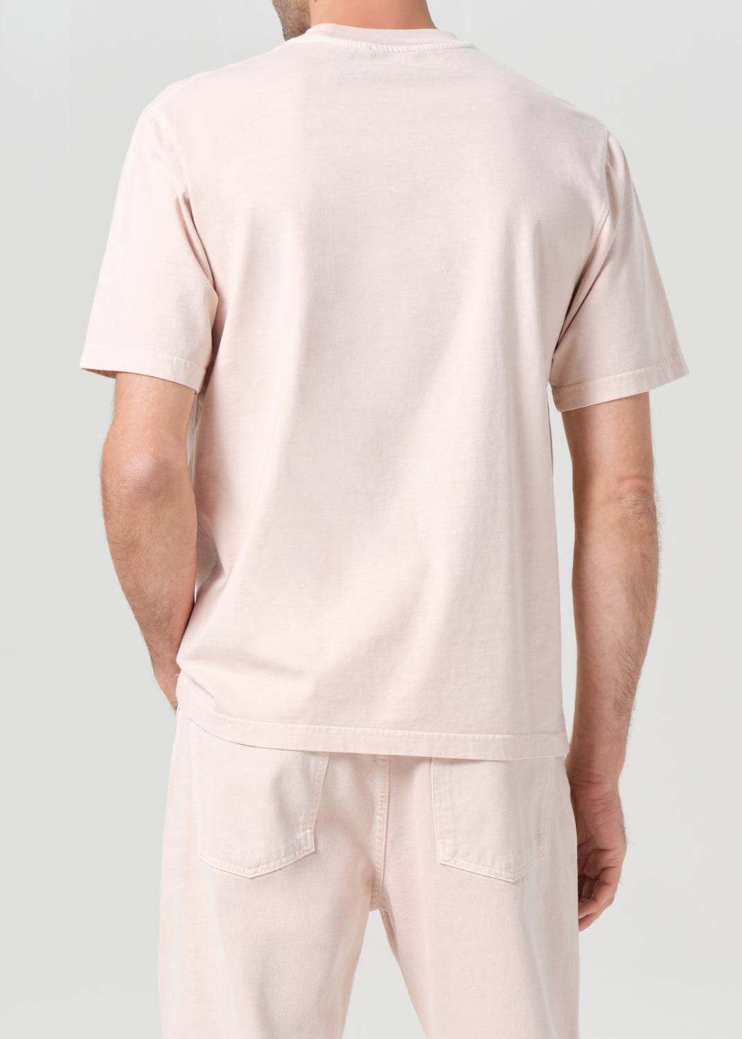 Person wearing a light pink t-shirt and pants on a plain background