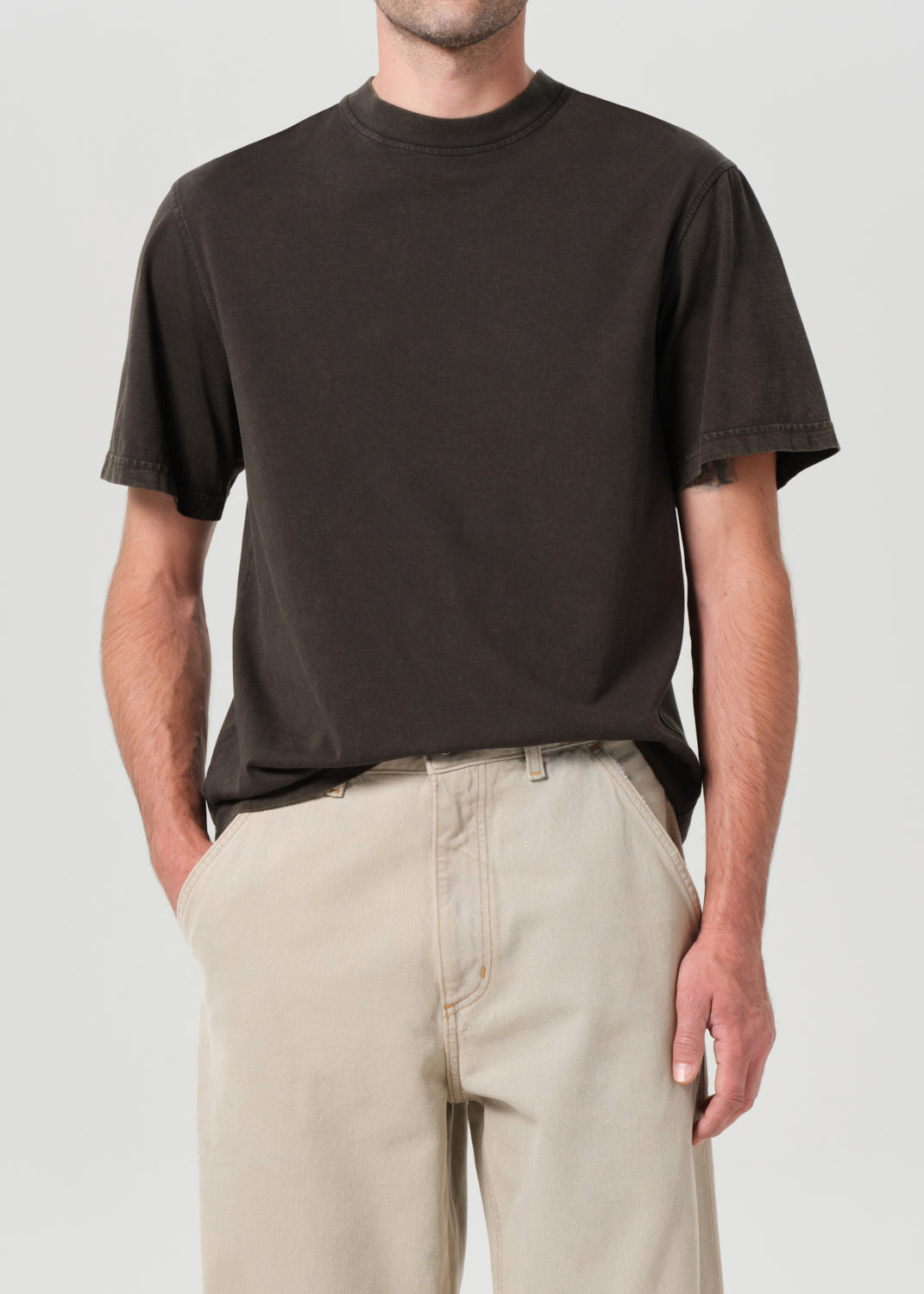 Person wearing a black t-shirt and beige pants against a plain background