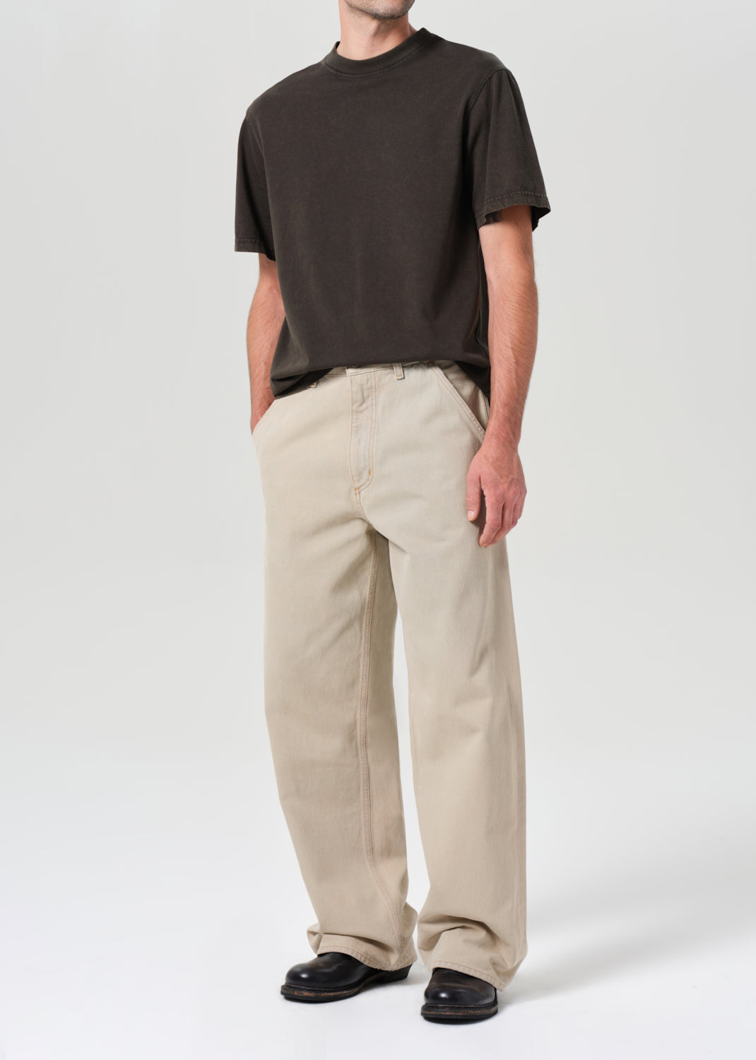 Person wearing a brown t-shirt and beige pants on a white background