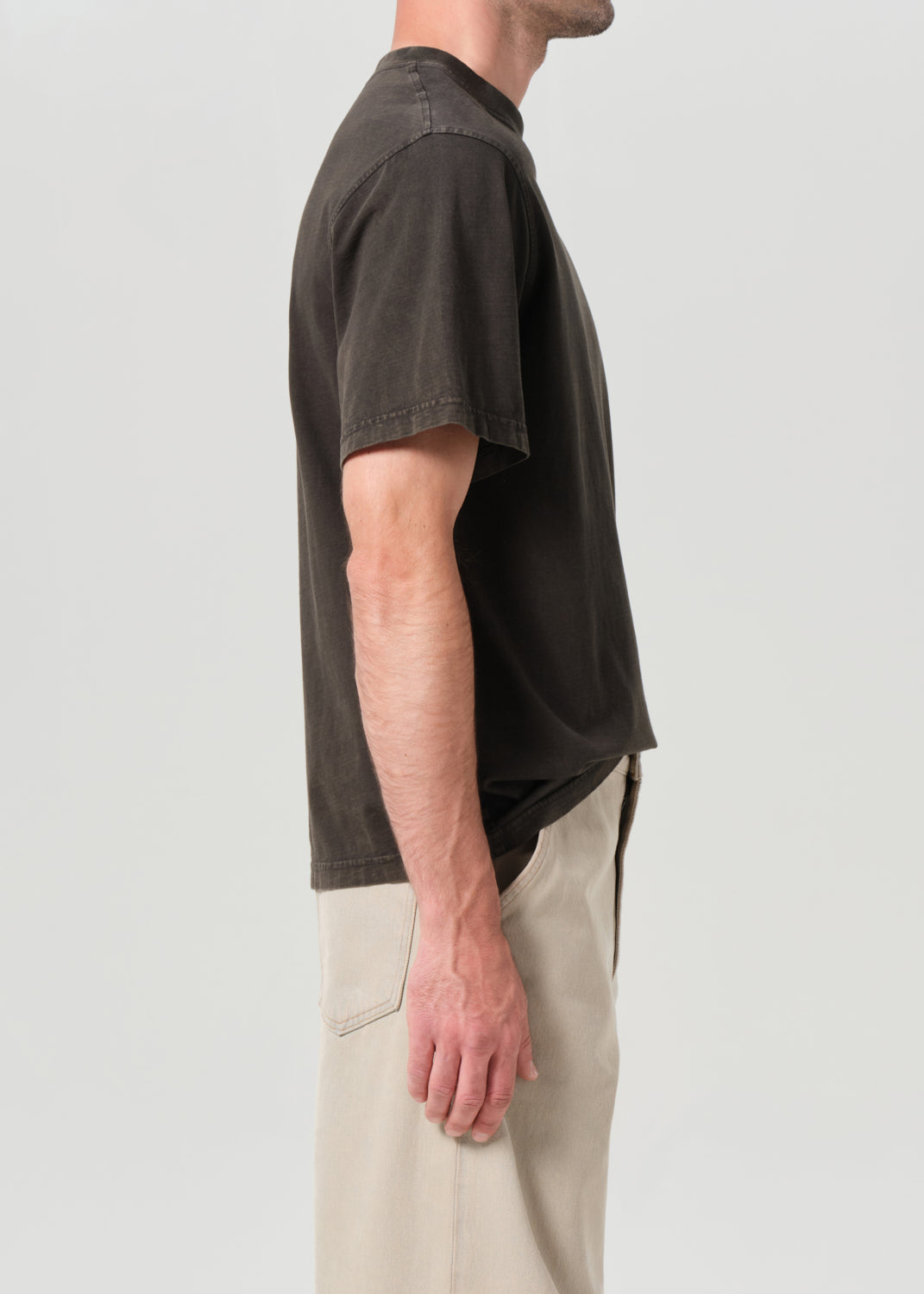 Person wearing a dark brown t-shirt and beige pants on a light gray background