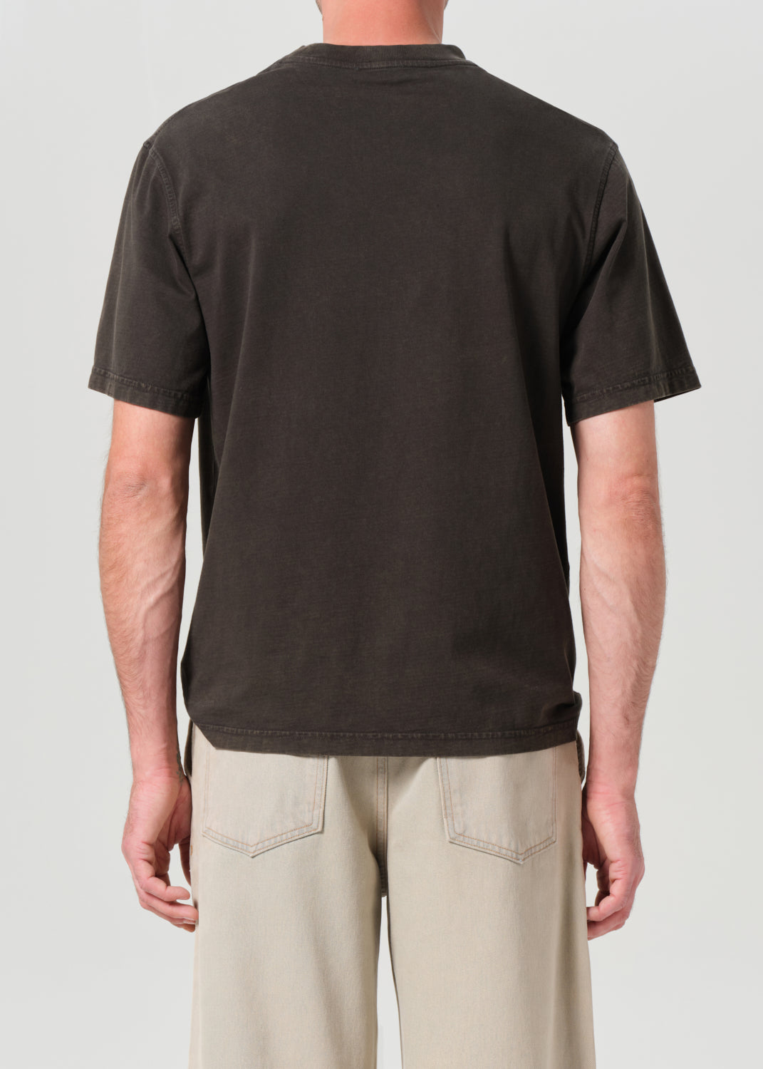 Person wearing a plain black t-shirt and beige pants on a light gray background