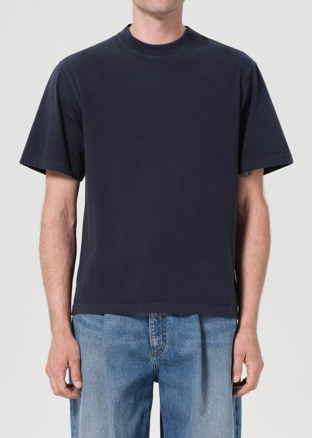 Person wearing a navy blue t-shirt and blue jeans on a plain background