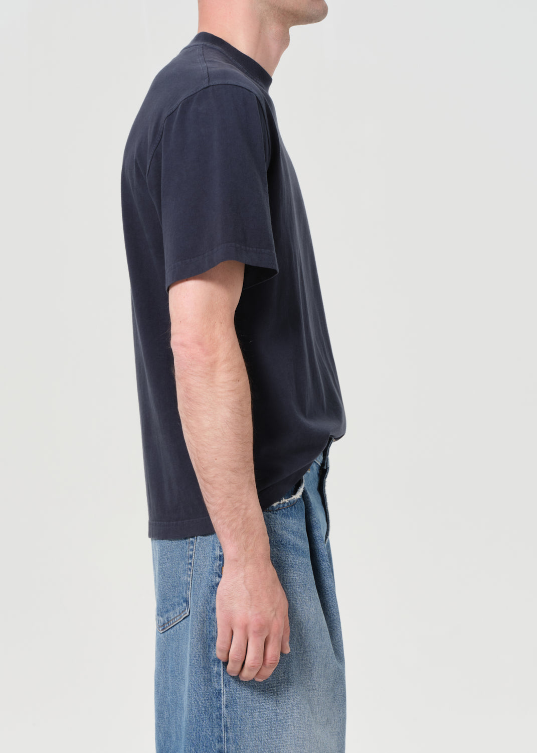 Person wearing a dark blue t-shirt and light blue jeans on a plain background