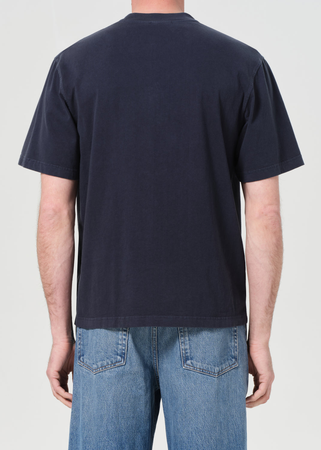 Person wearing a navy blue t-shirt and blue jeans on a plain background