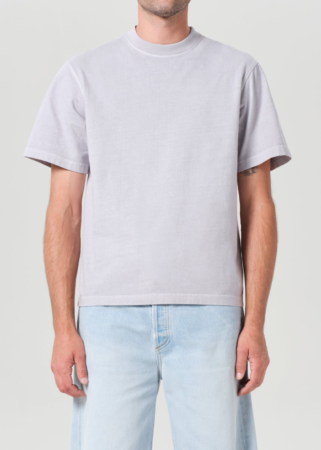 Person wearing a light gray t-shirt and light blue jeans on a plain background