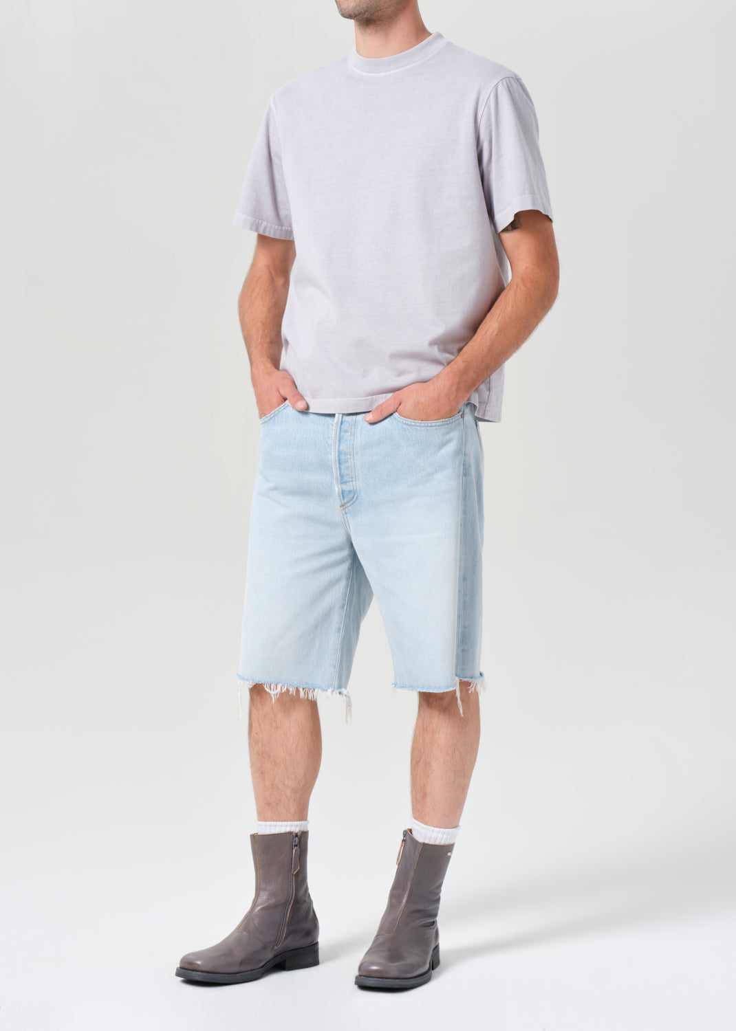 Person wearing light blue denim shorts and gray shoes on a white background