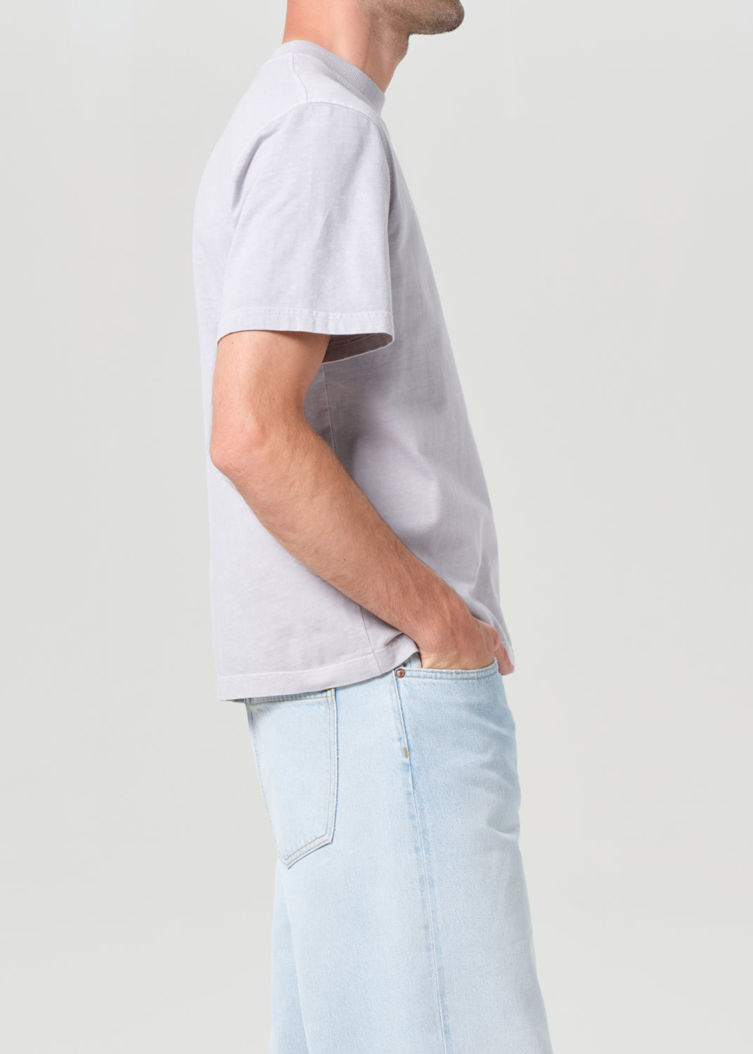 Person wearing a light gray t-shirt and light blue jeans on a plain background