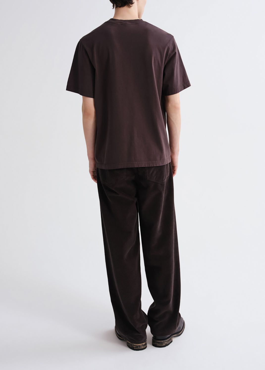 A person shown from the back wearing a dark brown short-sleeve t-shirt and matching dark brown corduroy pants against a grey background.