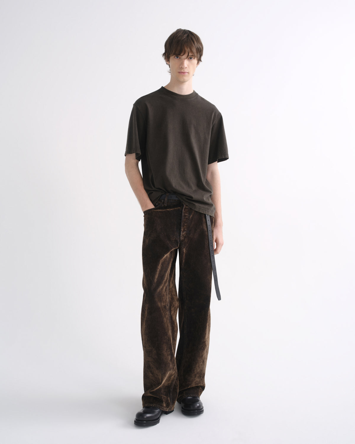 Person wearing a dark brown short sleeve T-shirt with dark brown pants, side view, on a grey background