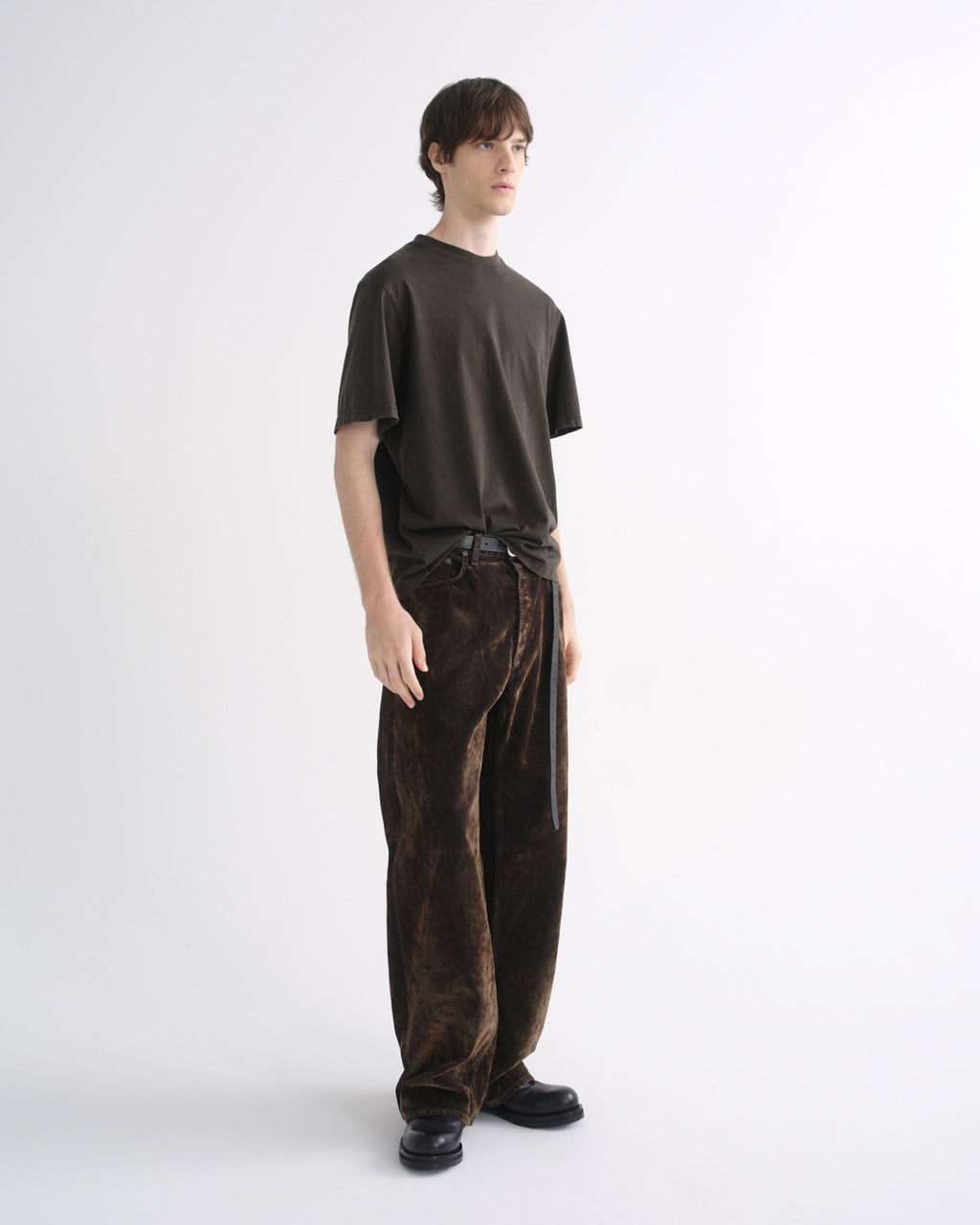 Person wearing a dark brown short sleeve T-shirt with dark brown pants on a grey background