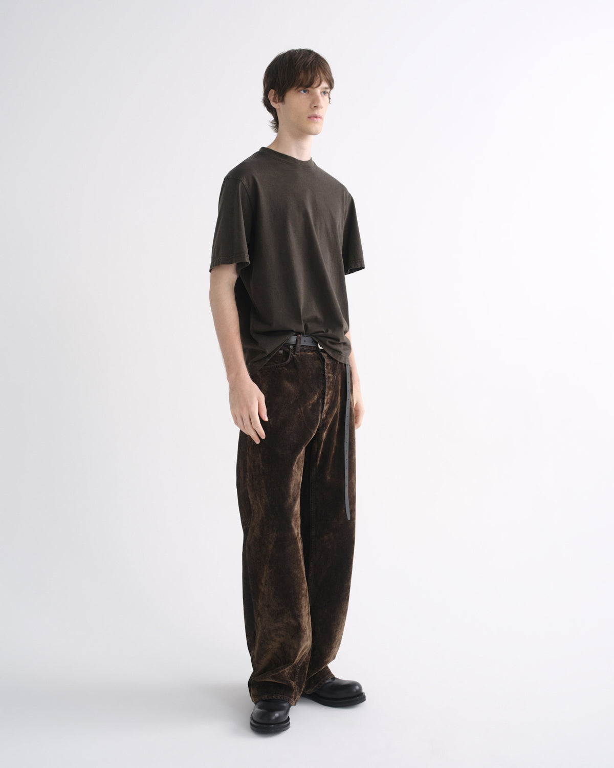 Person wearing a dark brown short sleeve T-shirt with dark brown pants on a grey background