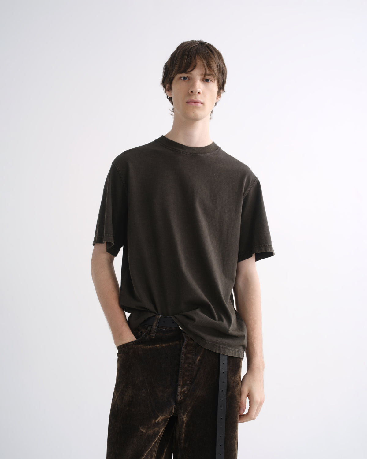 Person wearing a dark brown short sleeve T-shirt with dark brown pants on a grey background
