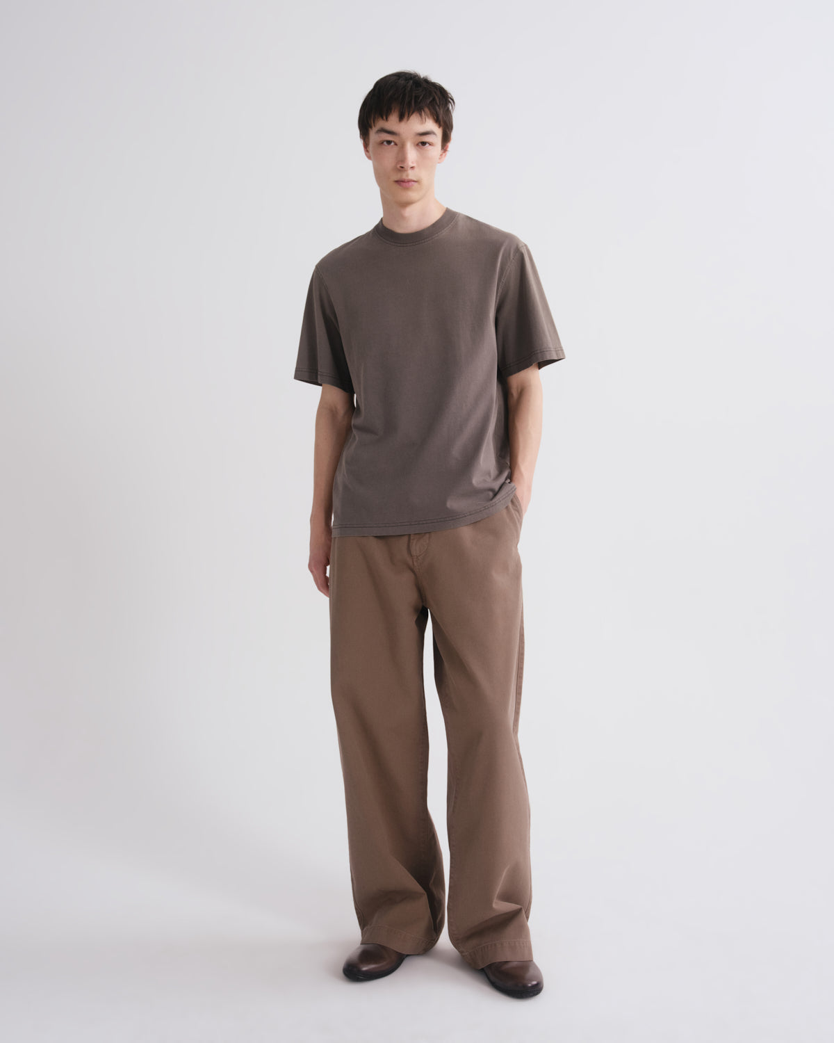 Man wearing a brown t-shirt and pants on a white background