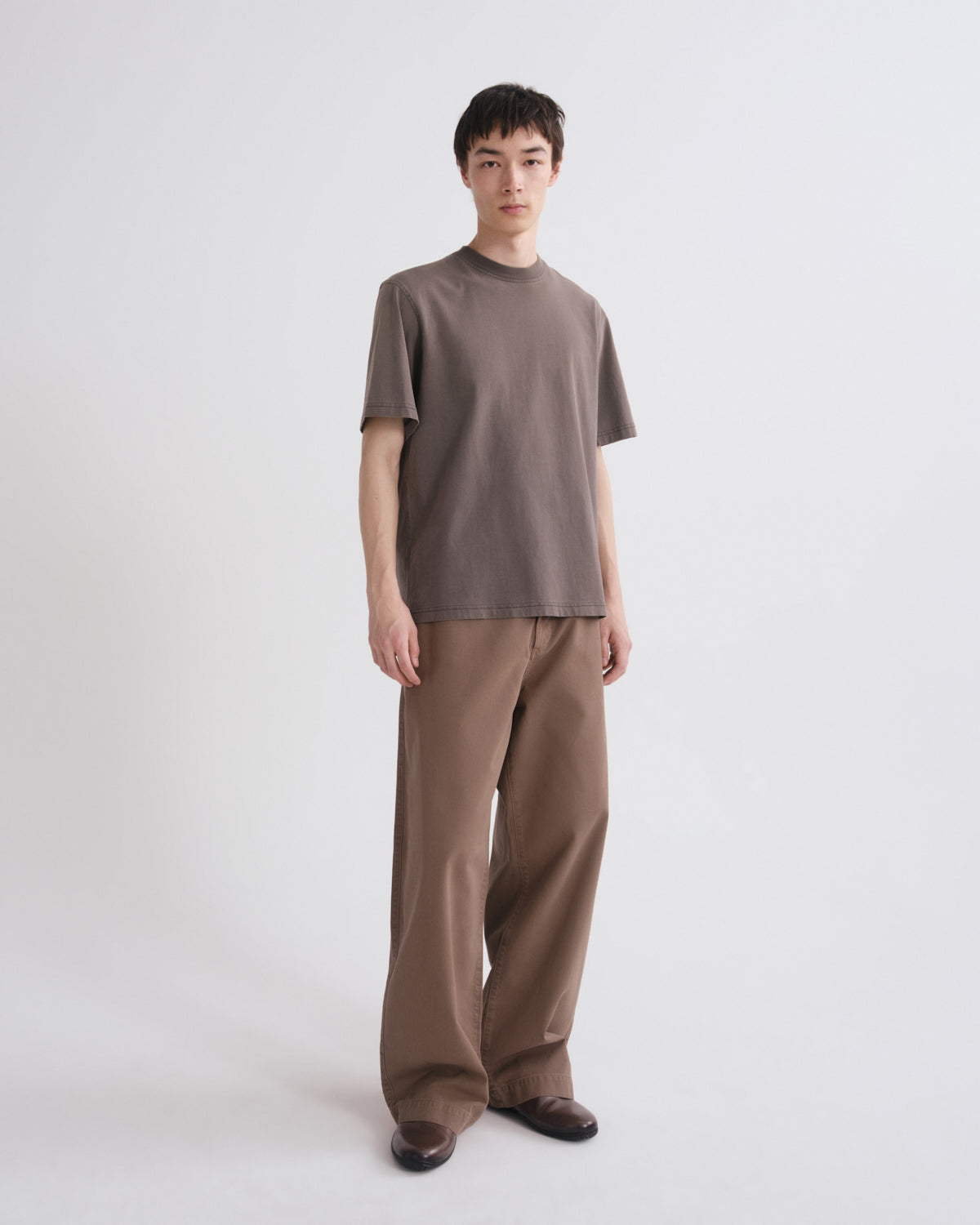 Person wearing a brown t-shirt and pants on a white background