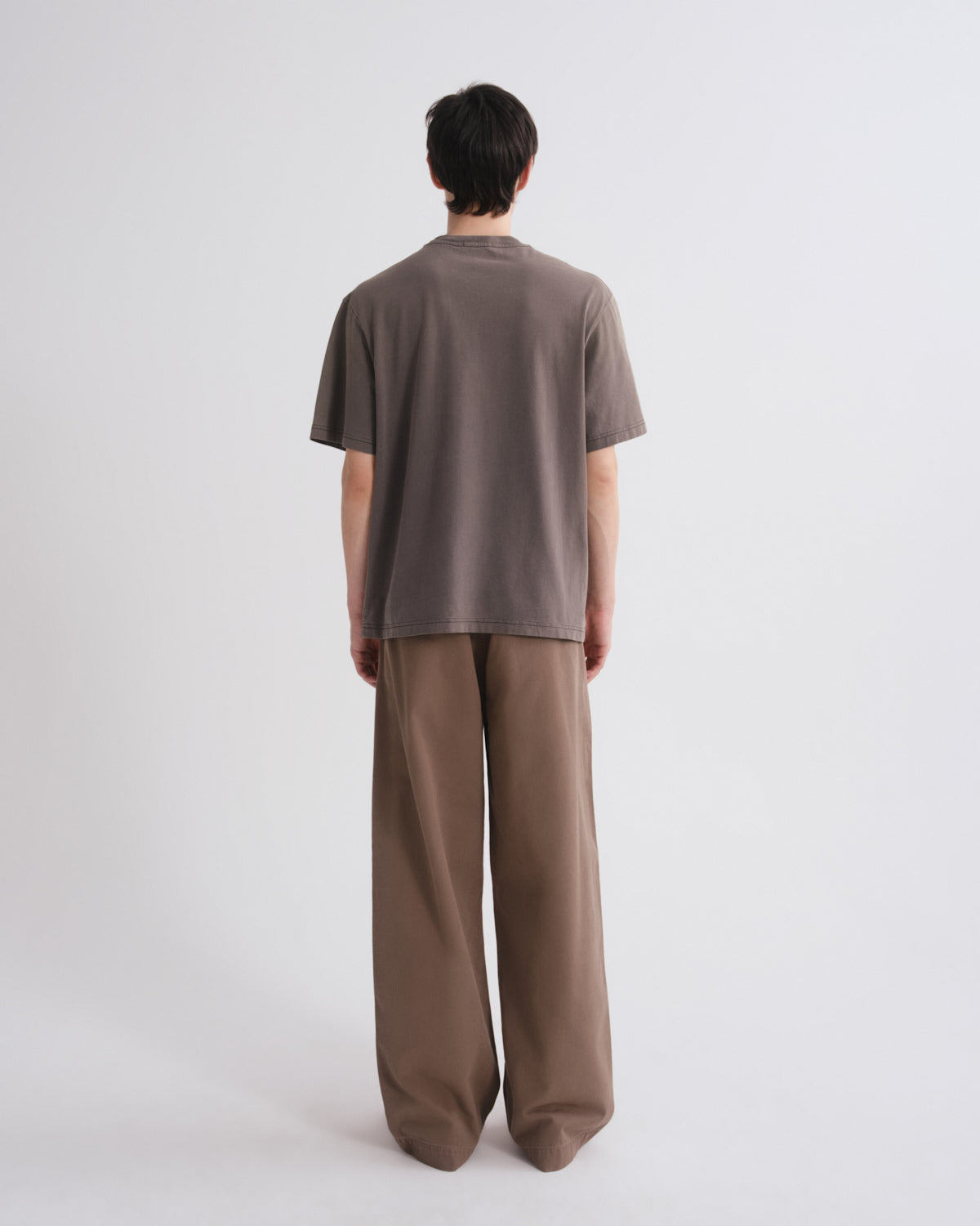 Person wearing a brown t-shirt and wide-leg pants on a white background