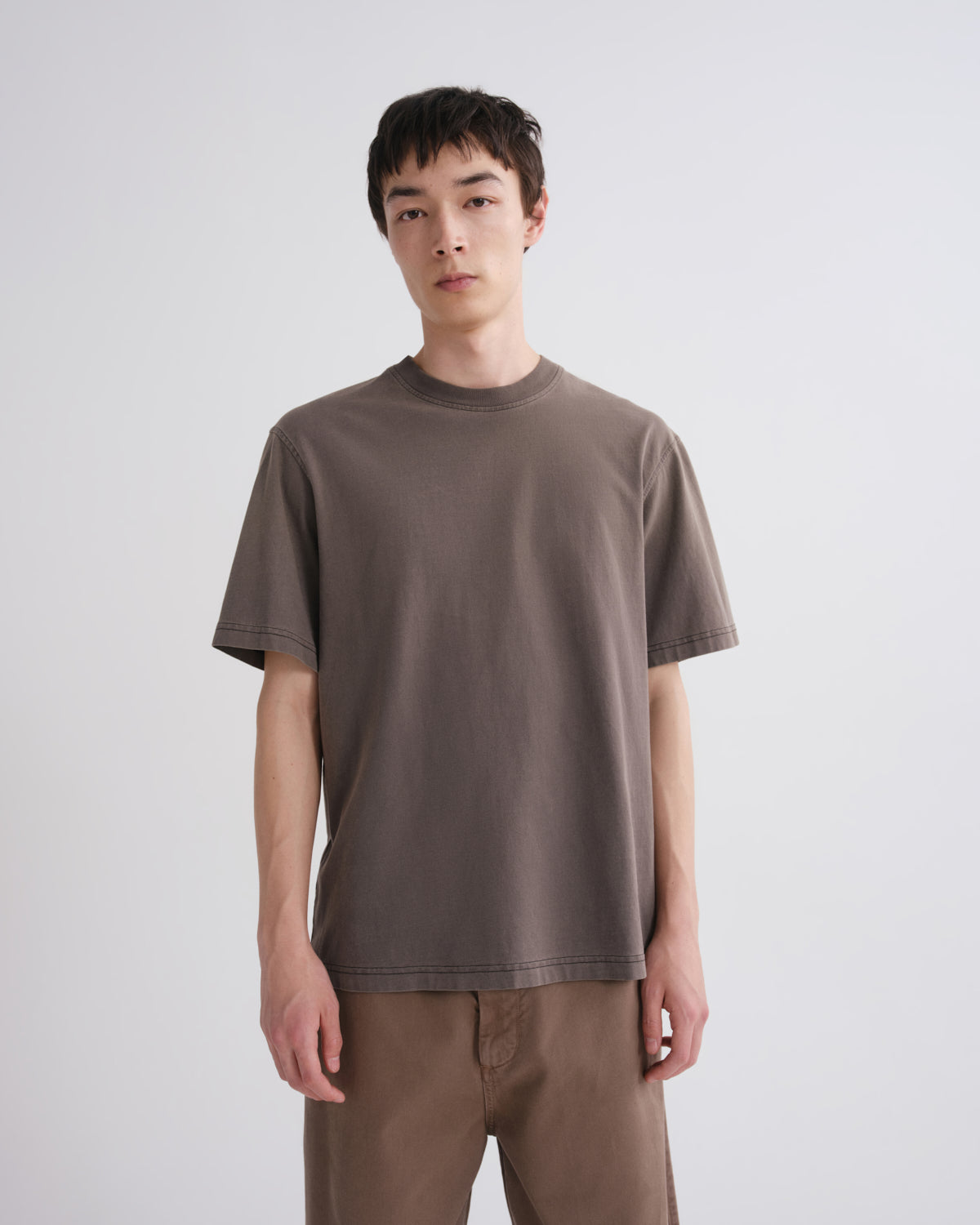 Person wearing a brown t-shirt and pants on a plain background