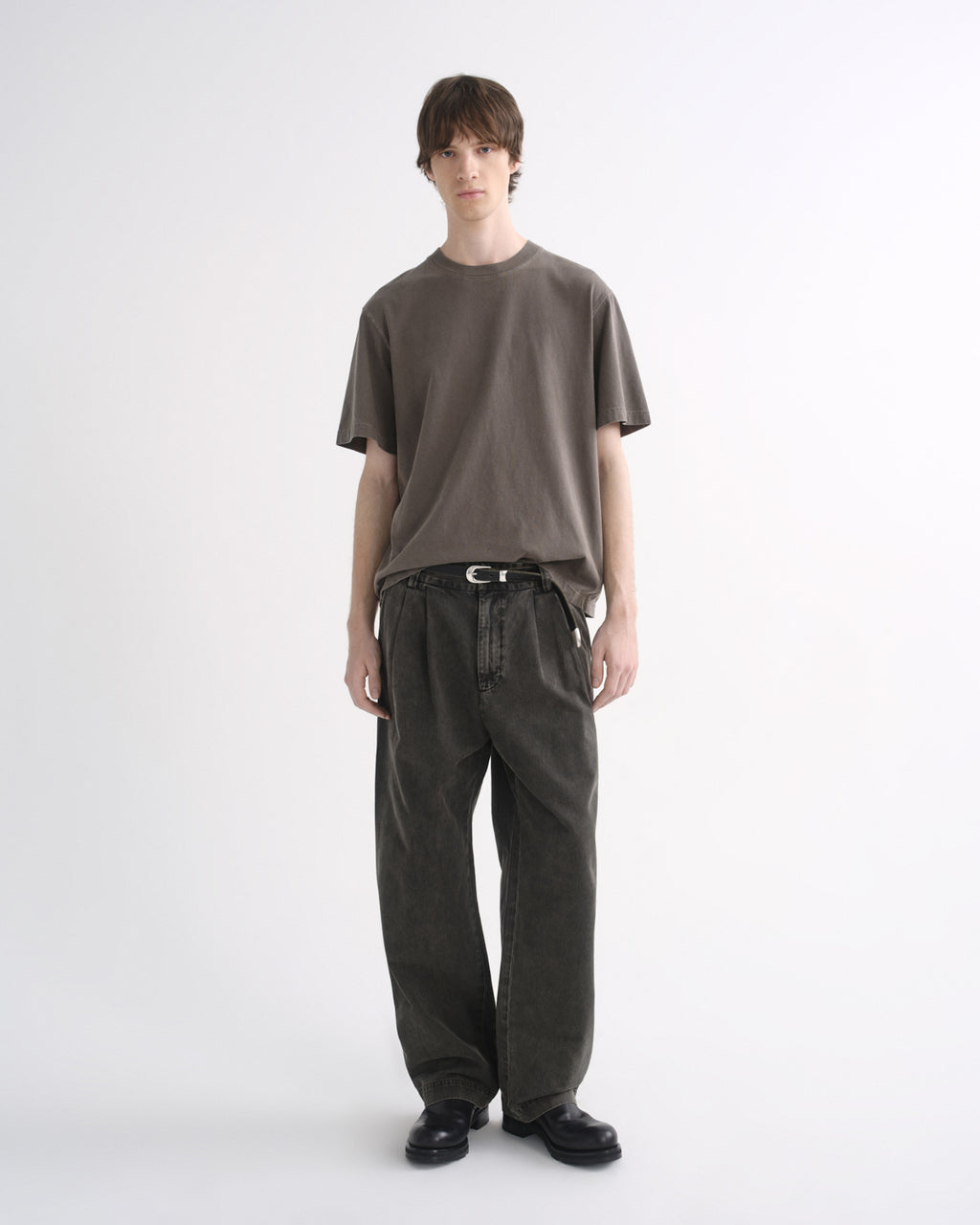 Person wearing a grey short sleeve T-shirt with dark pants and black shoes on a grey background