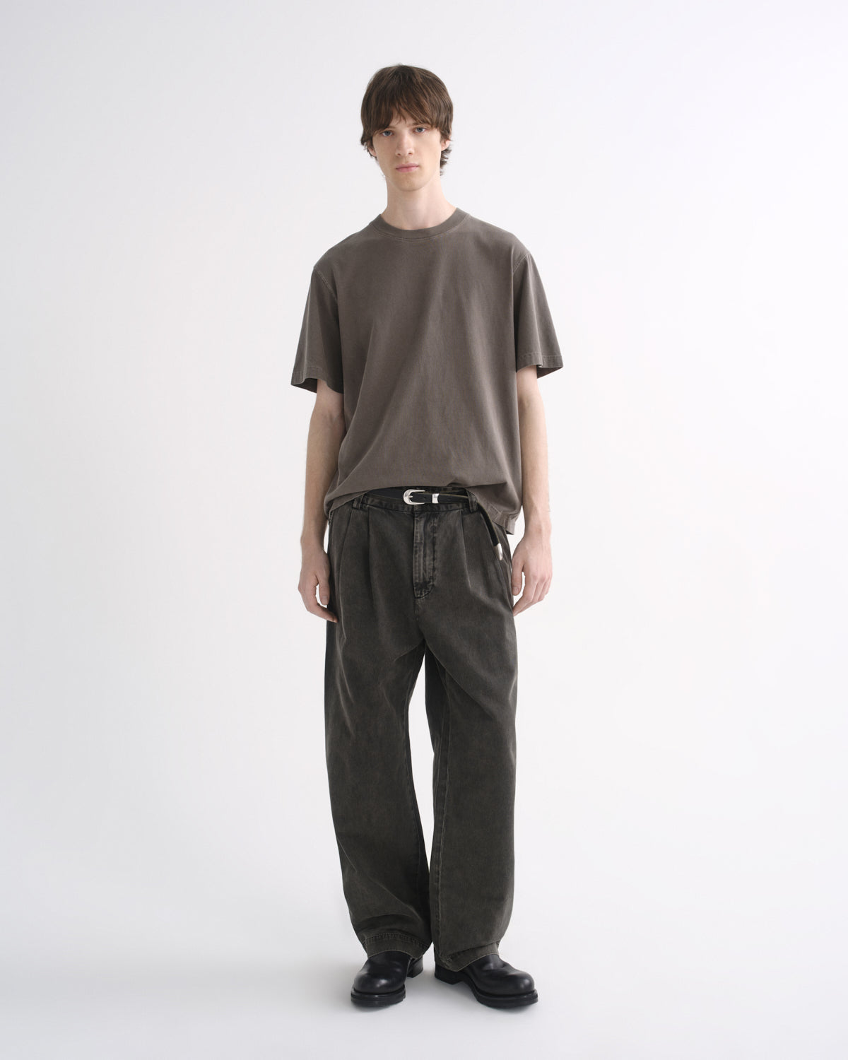 Person wearing a grey short sleeve T-shirt with dark pants and black shoes on a grey background