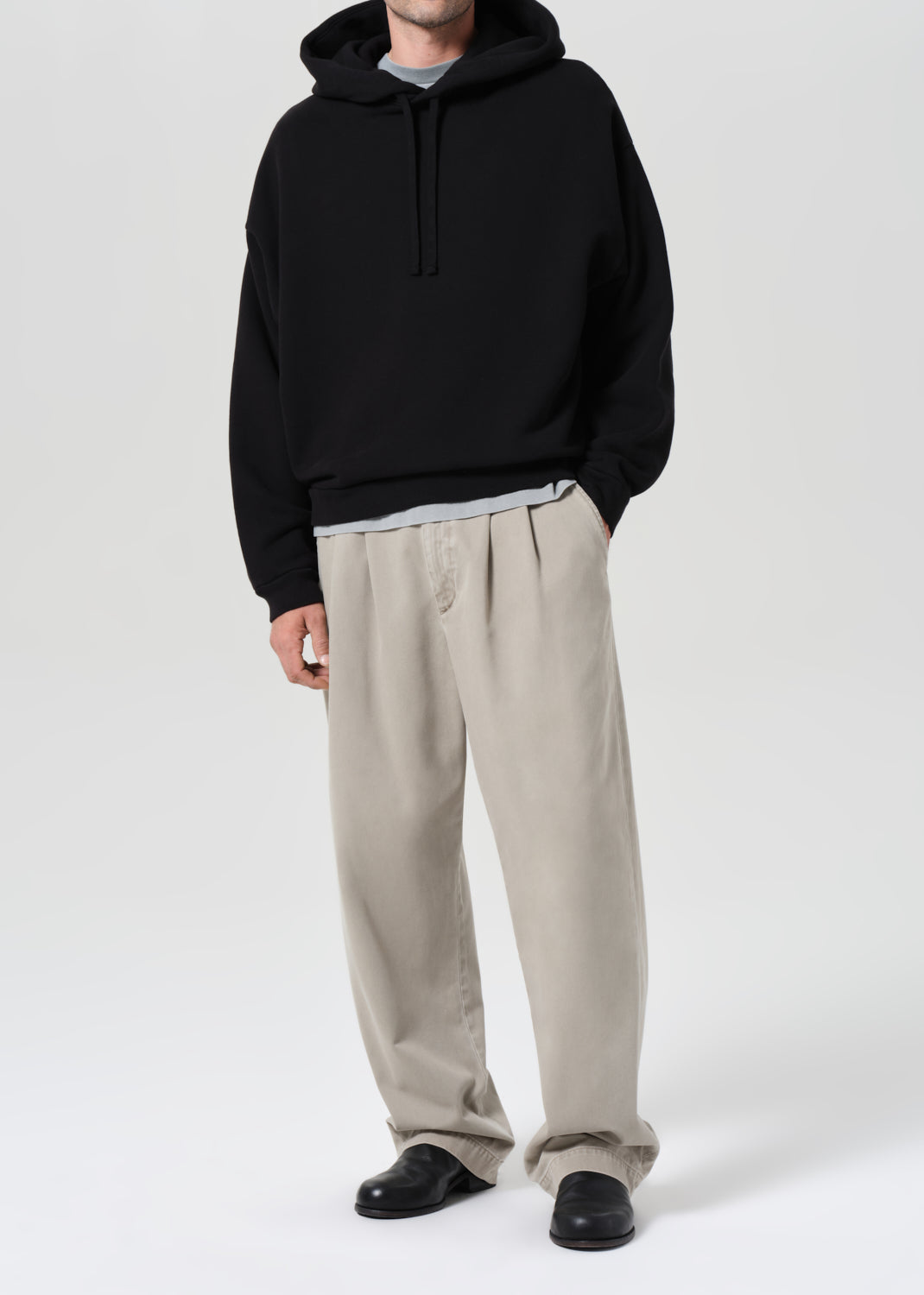 Person wearing a black hoodie and beige pants on a white background